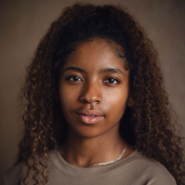 Young woman with long curly hair looking directly at the camera with a calm expression