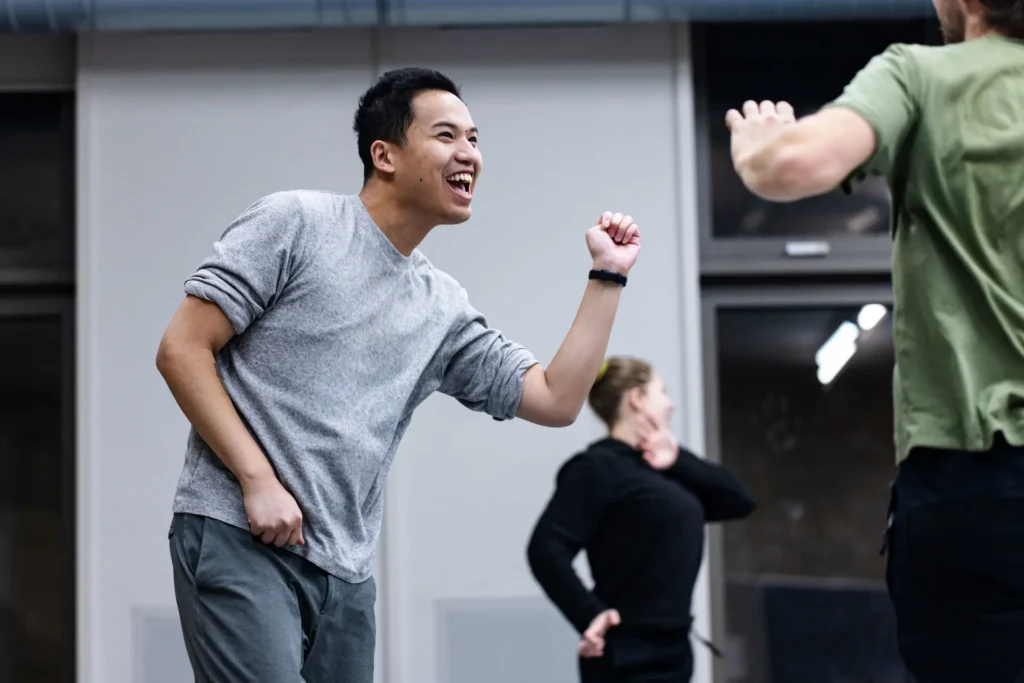 Man cheering with a raised fist during a rehearsal, with others in the background
