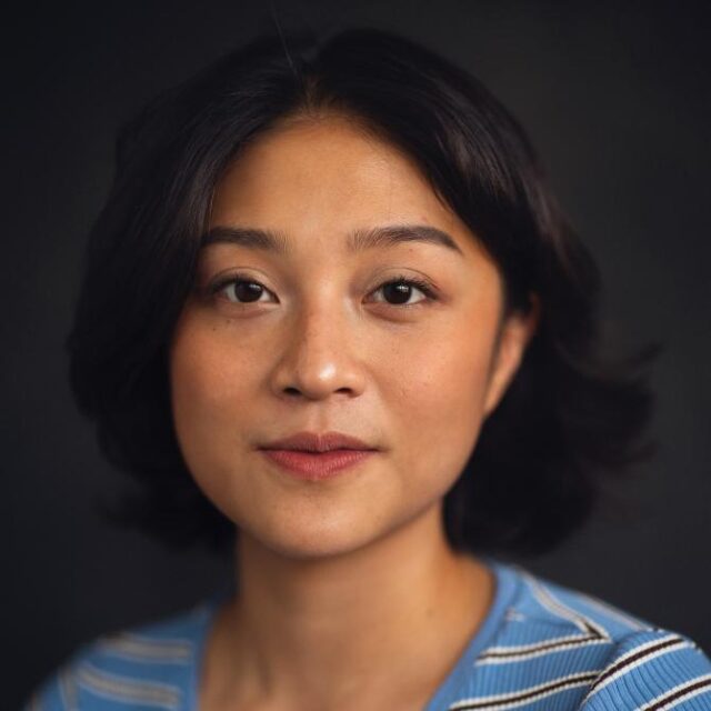 Portrait of a woman with shoulder-length dark hair, wearing a blue striped top, against a dark background