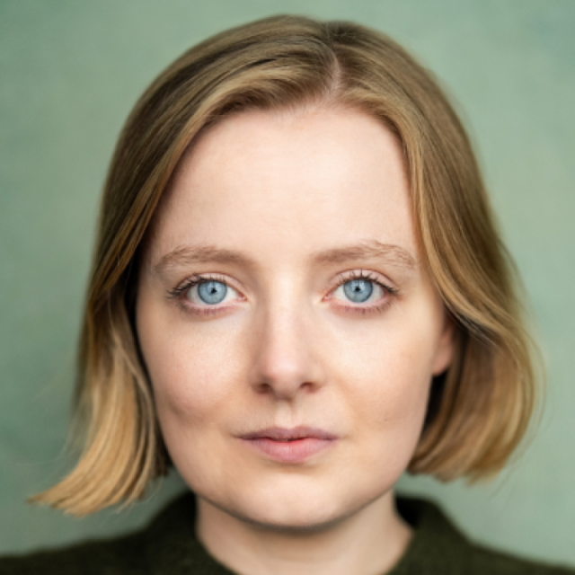 Studio portrait of a woman with shoulder-length blonde hair and blue eyes, facing the camera against a green background