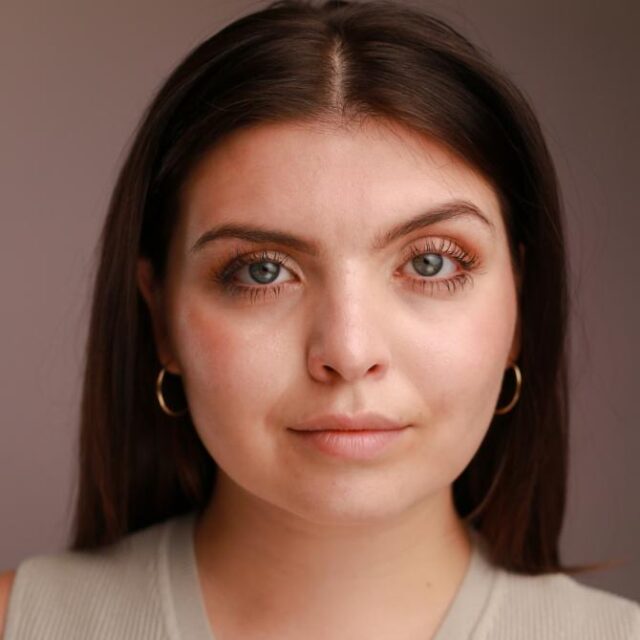 Close-up portrait of a young woman with long dark hair, hoop earrings and blue eyes, looking directly at the camera