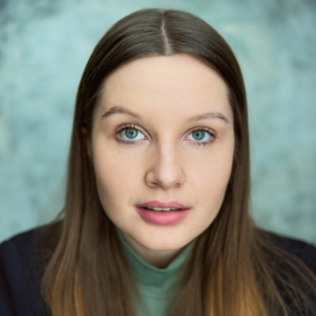 Close-up portrait of a young woman with long brown hair and green eyes, wearing a green top