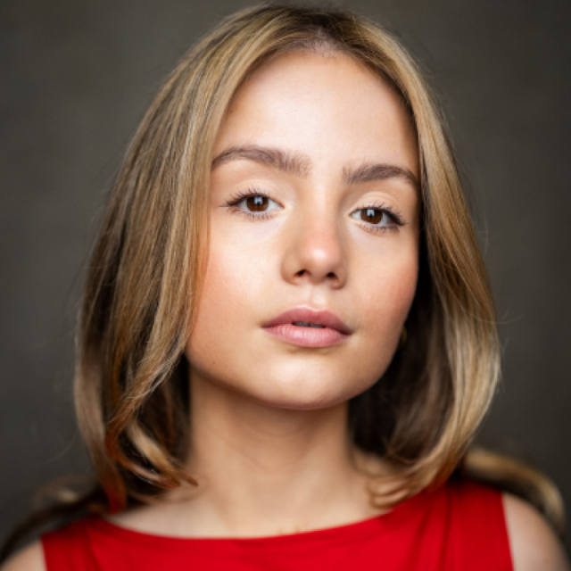 Close-up portrait of a young woman with shoulder-length blonde hair, wearing a red top, against a dark background