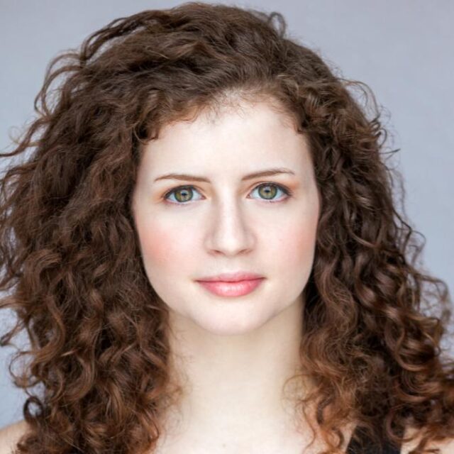 Close-up portrait of a woman with long curly brown hair and green eyes, facing the camera
