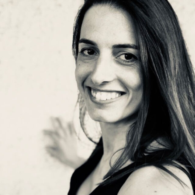 Black-and-white portrait of a smiling woman with long dark hair, looking over her shoulder