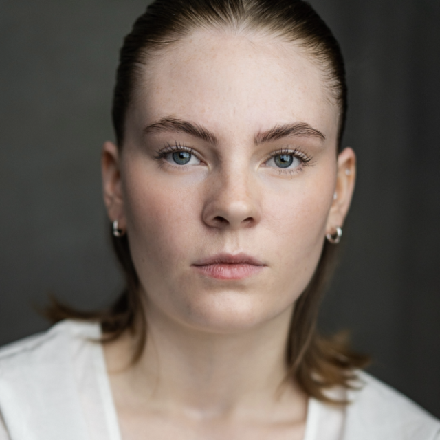 Close-up portrait of a young woman with fair skin, blue eyes and reddish-brown hair, looking directly at the camera