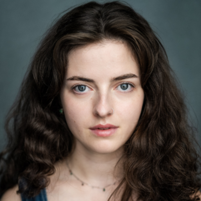 Close-up portrait of a young woman with curly brown hair and blue eyes, looking directly at the camera