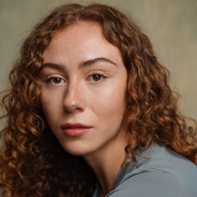 Close-up portrait of a young woman with curly auburn hair looking directly at the camera