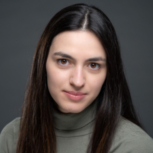 Portrait of a woman with long dark hair, wearing a grey polo neck jumper, against a grey background