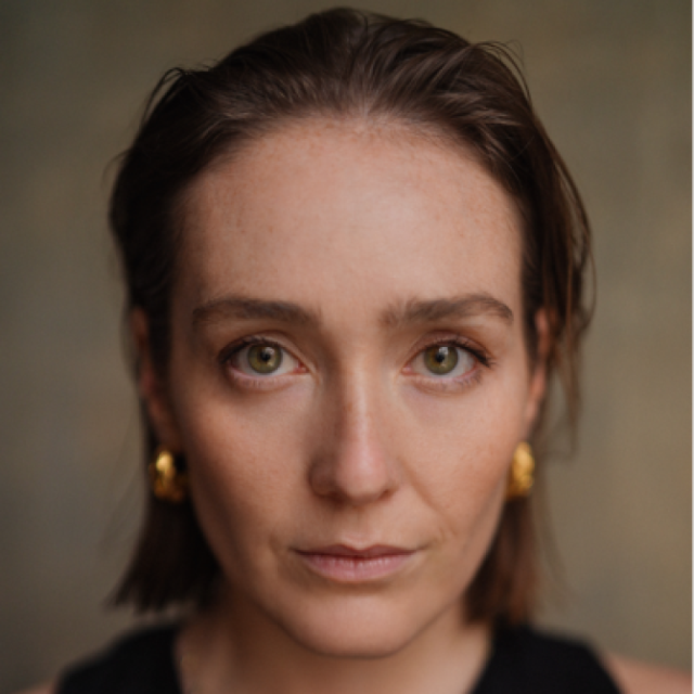 Close-up portrait of a woman with green eyes and gold earrings, looking directly at the camera