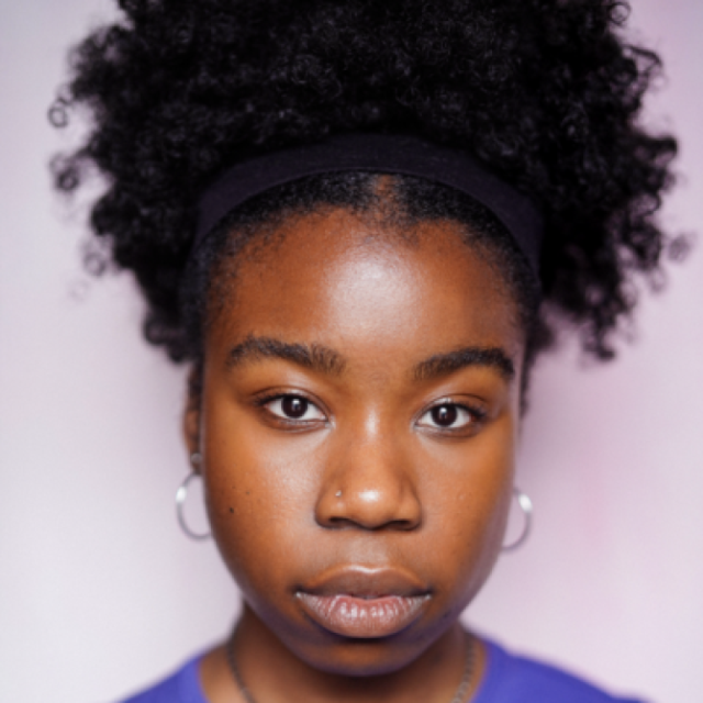 Close-up portrait of a young woman with curly hair pulled back, wearing hoop earrings and a black headband