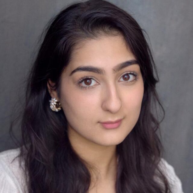 Close-up portrait of a young woman with long dark hair, wearing a decorative earring and a light-coloured top