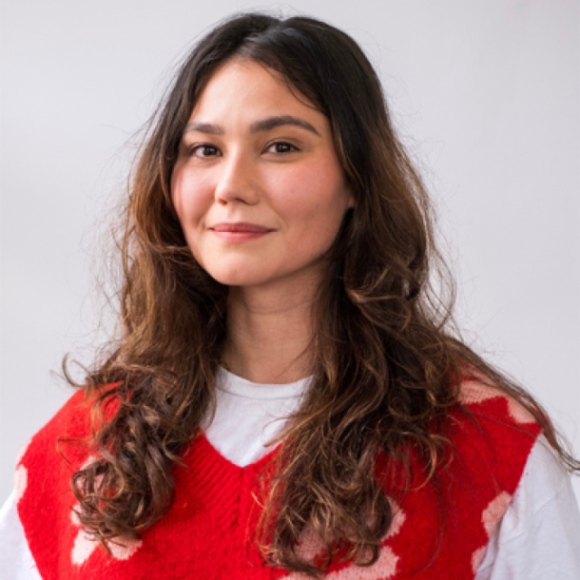 Woman with long wavy brown hair wearing a red and white patterned jumper over a white top
