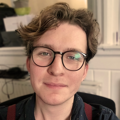 Portrait of a young man with curly brown hair and glasses, smiling slightly