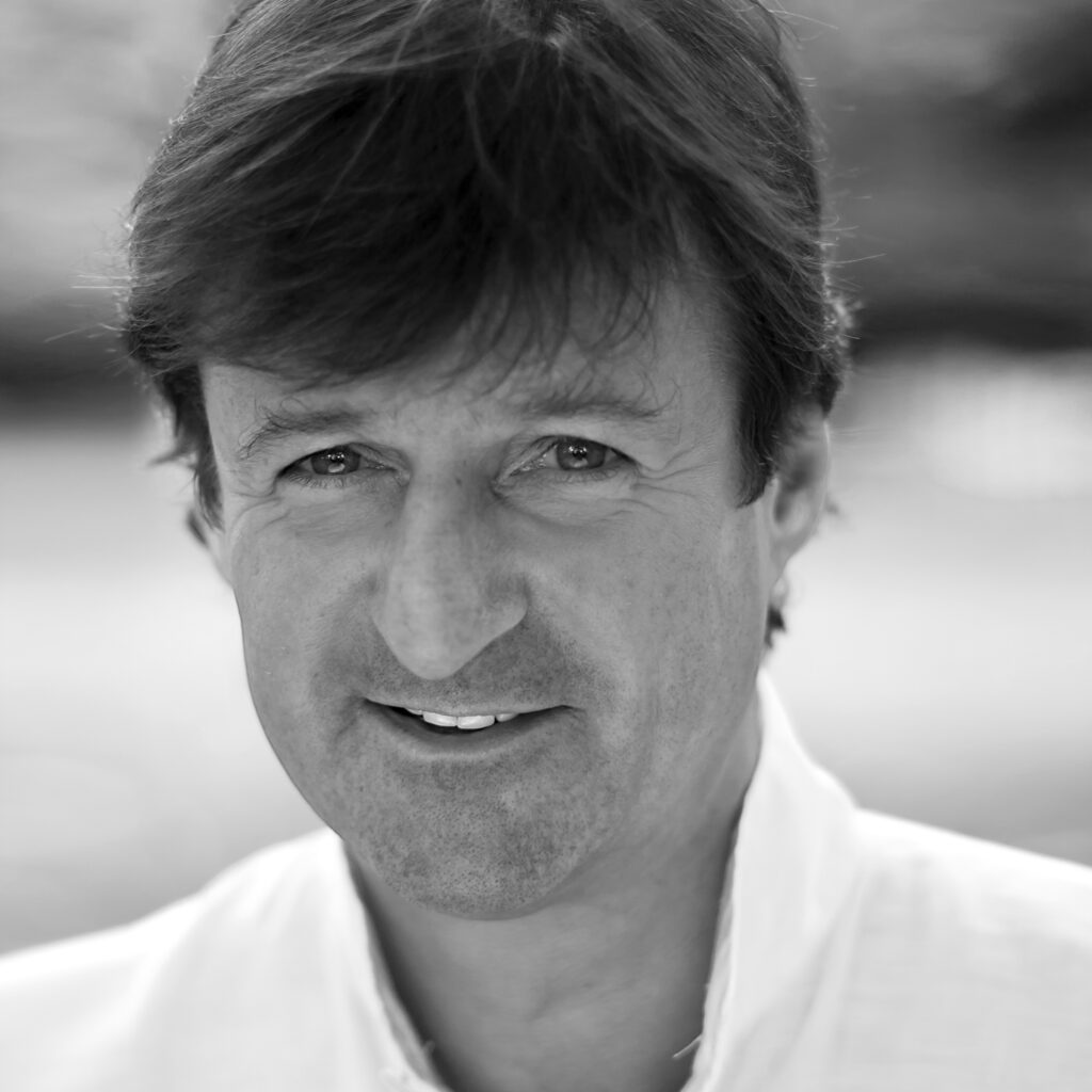 Black and white close-up portrait of a middle-aged man with dark hair, smiling at the camera in an open-collared shirt