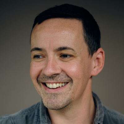 Headshot of a smiling man with short dark hair, wearing a grey collared shirt