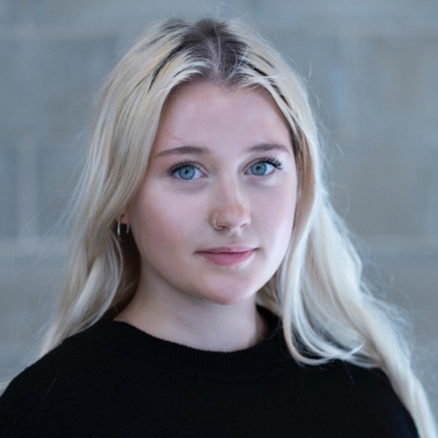 Young woman with long blonde hair and blue eyes, wearing a black top, looking directly at the camera