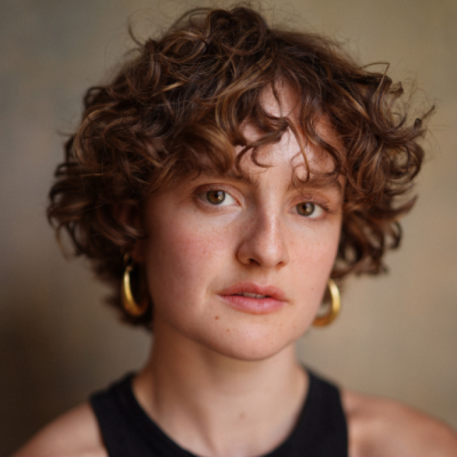 Close-up portrait of a young woman with curly brown hair and gold hoop earrings, looking directly at the camera