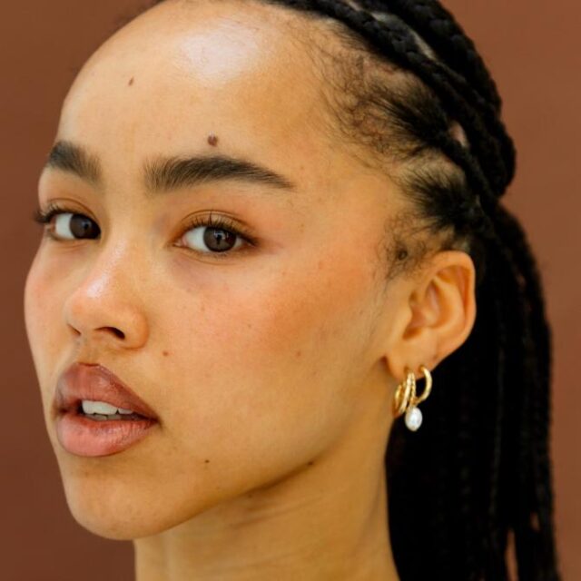 Close-up of a woman with braided hair, natural makeup and gold hoop earrings with a pearl drop