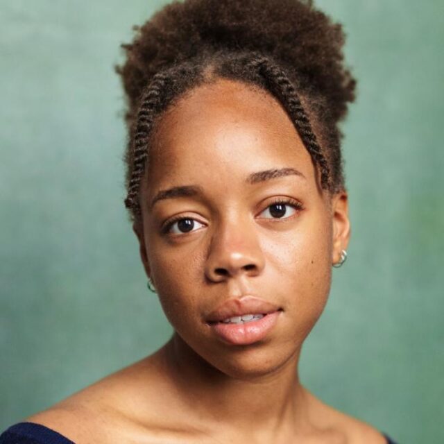 Portrait of a woman with braided hair pulled back, looking directly at the camera against a green background