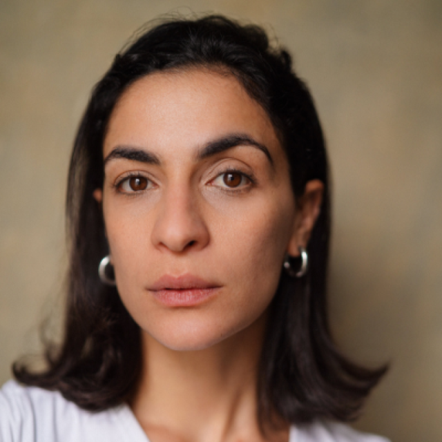 Close-up portrait of a woman with dark hair and hoop earrings, looking directly at the camera with a neutral expression