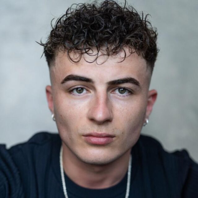 Young man with curly dark hair and earrings, looking directly at the camera