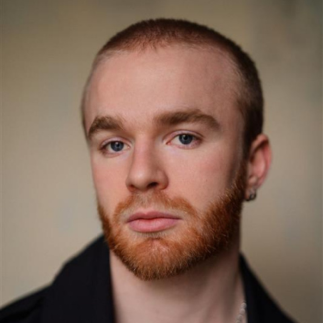Close-up portrait of a young man with short red hair, blue eyes and a full red beard, wearing a dark shirt