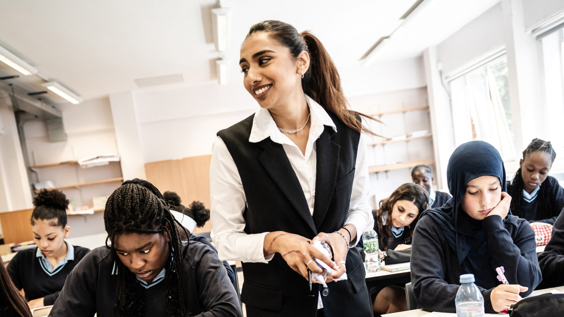 A teacher stands in a classroom with a group of learners working at desks