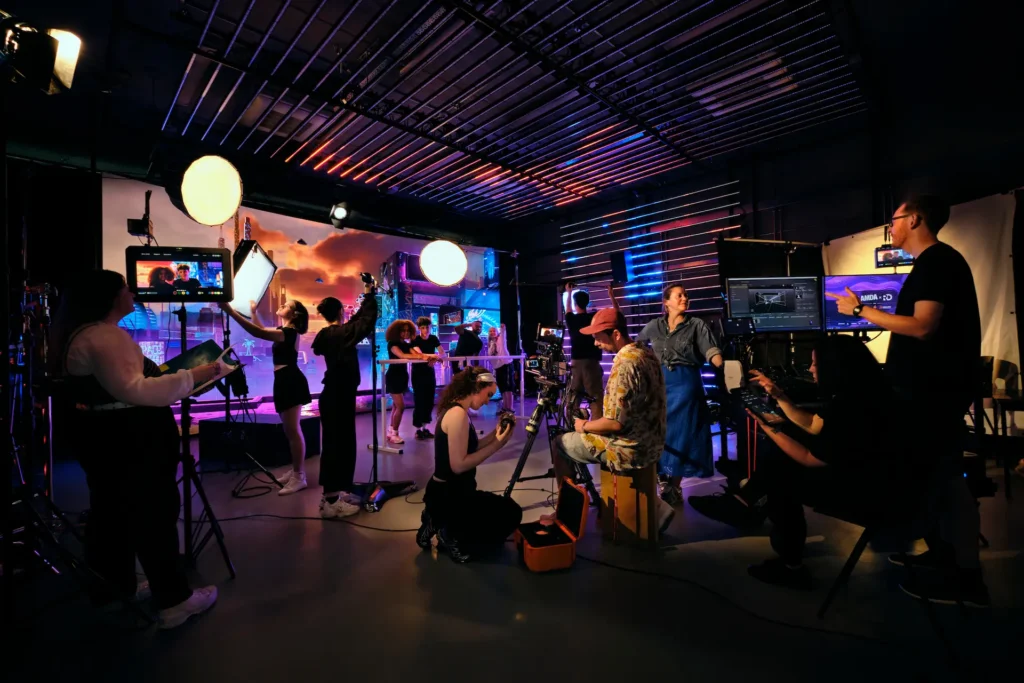 Film crew on set adjusting lighting and cameras, with actors performing in front of a neon cityscape backdrop