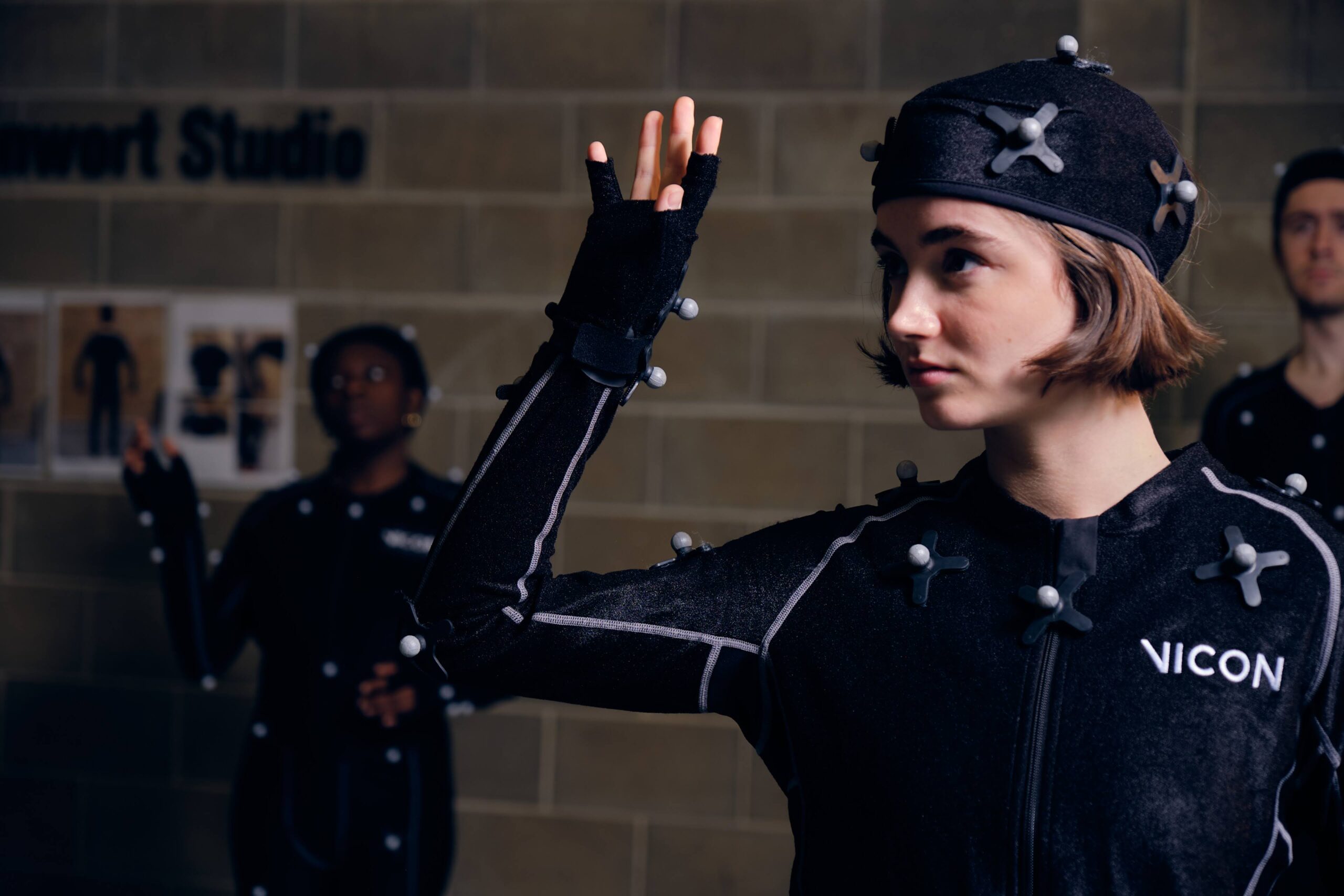 A woman in a black motion capture suit raises their right hand